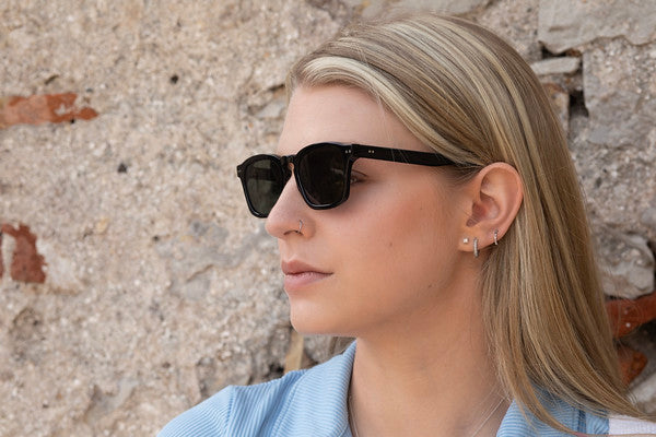 Woman in Genoa Black sunglasses with green lenses looking to the side.