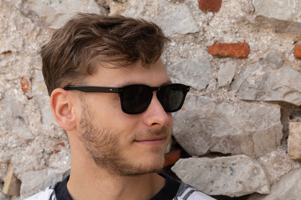 Man in Genoa Black sunglasses with green lenses looking to the side.